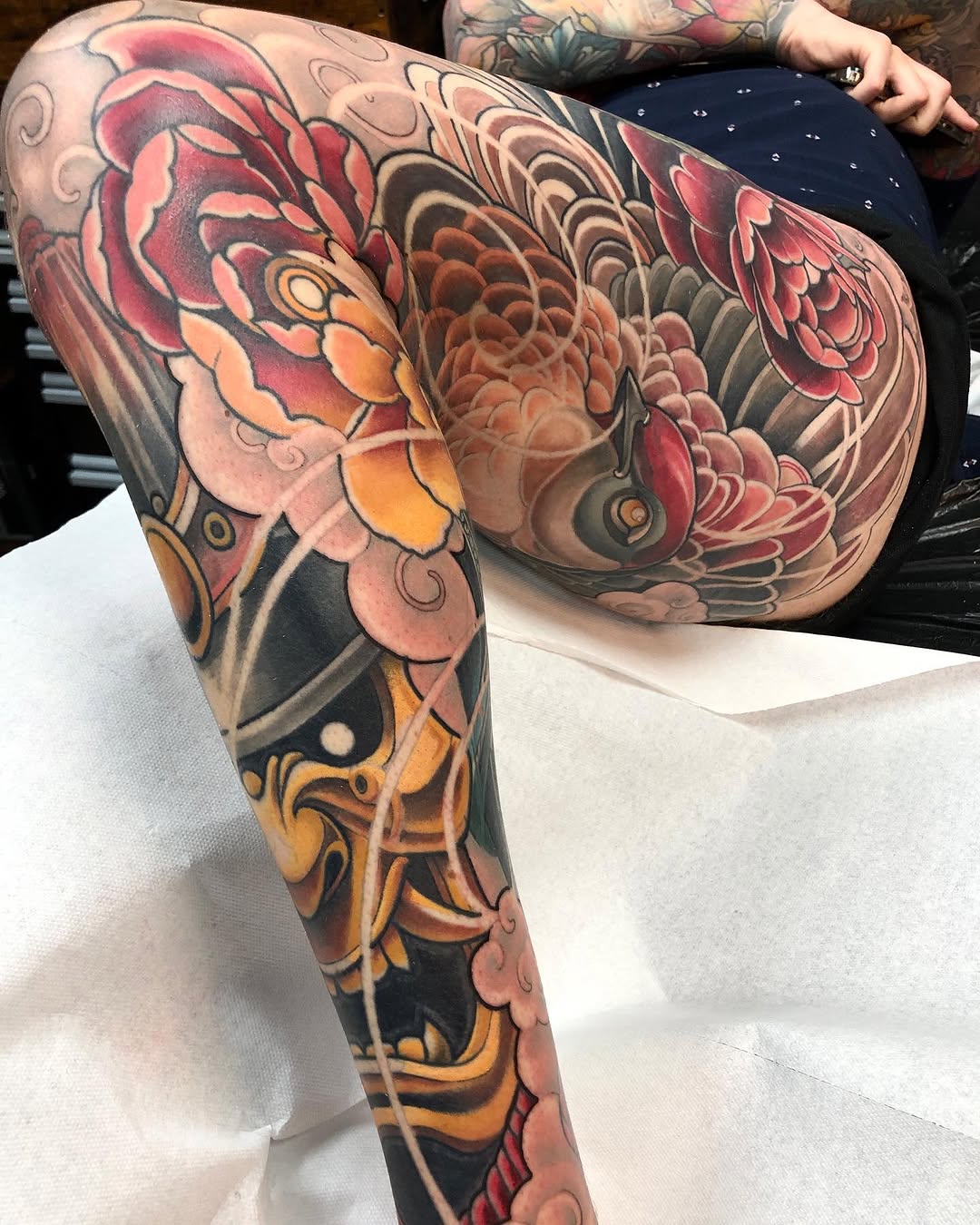 Colorful full-leg sleeve tattoo featuring red, pink, orange, and black layered floral and ornamental designs covering the thigh and calf.