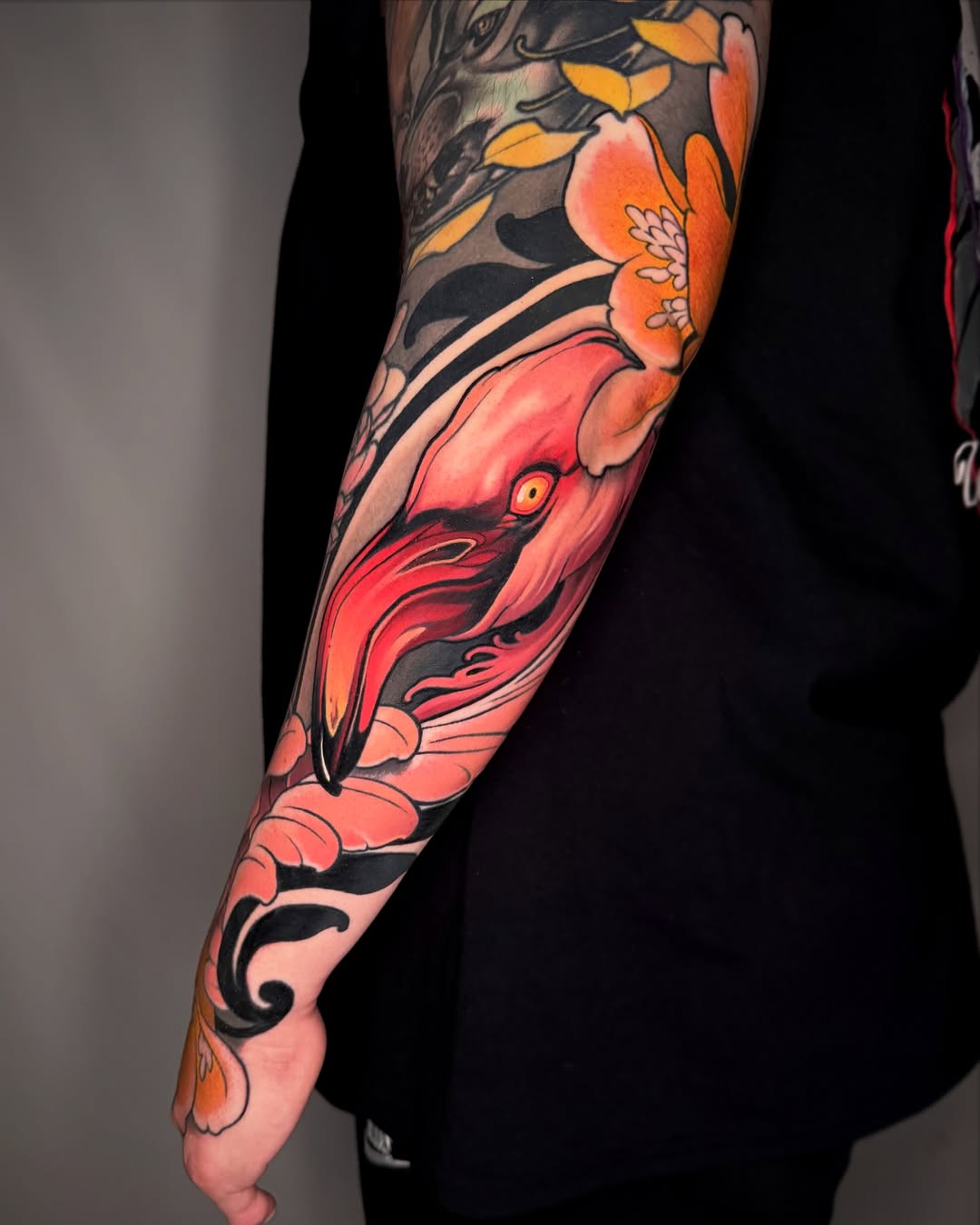 Full-arm sleeve tattoo featuring a red bird with orange flowers and dark foliage, displaying vibrant coral and black ink on the wearer's arm.