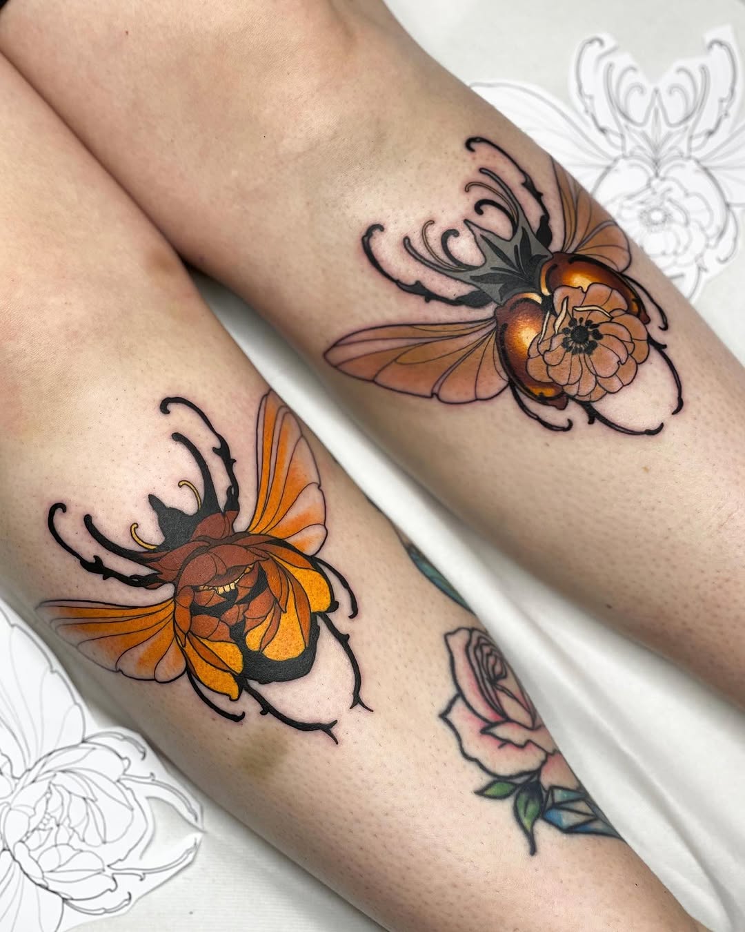 Two colorful beetles with orange and black wings and curved antennae tattooed on the forearm, with sketch designs visible in the background.