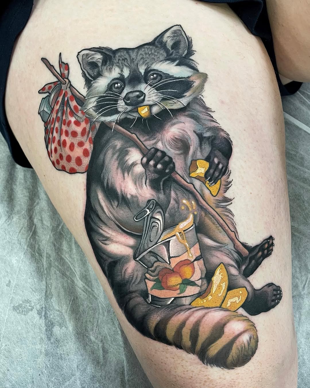 Colorful tattoo on thigh of a raccoon holding a bag of strawberries and wearing clothing with fruit designs, featuring red, yellow, and grey tones.