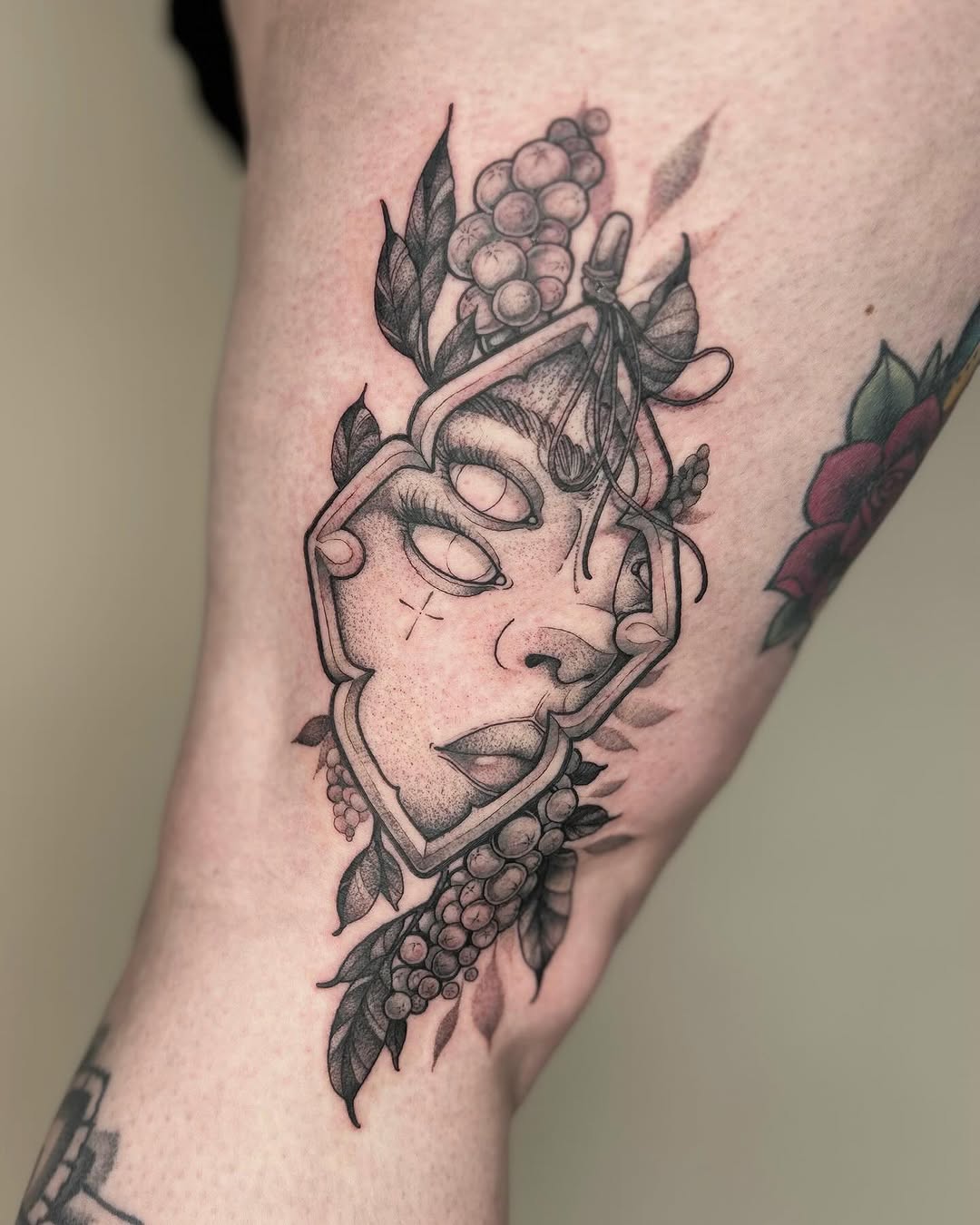 Decorative head sculpture with closed eyes and grapes adorning the sides, rendered in black and gray ink on the calf.