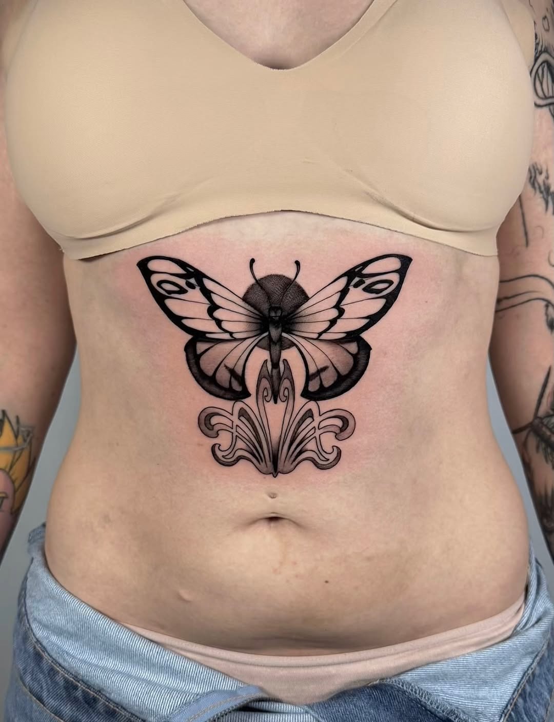 Butterfly with ornamental flourish design tattooed on chest in black ink with shaded detailing.