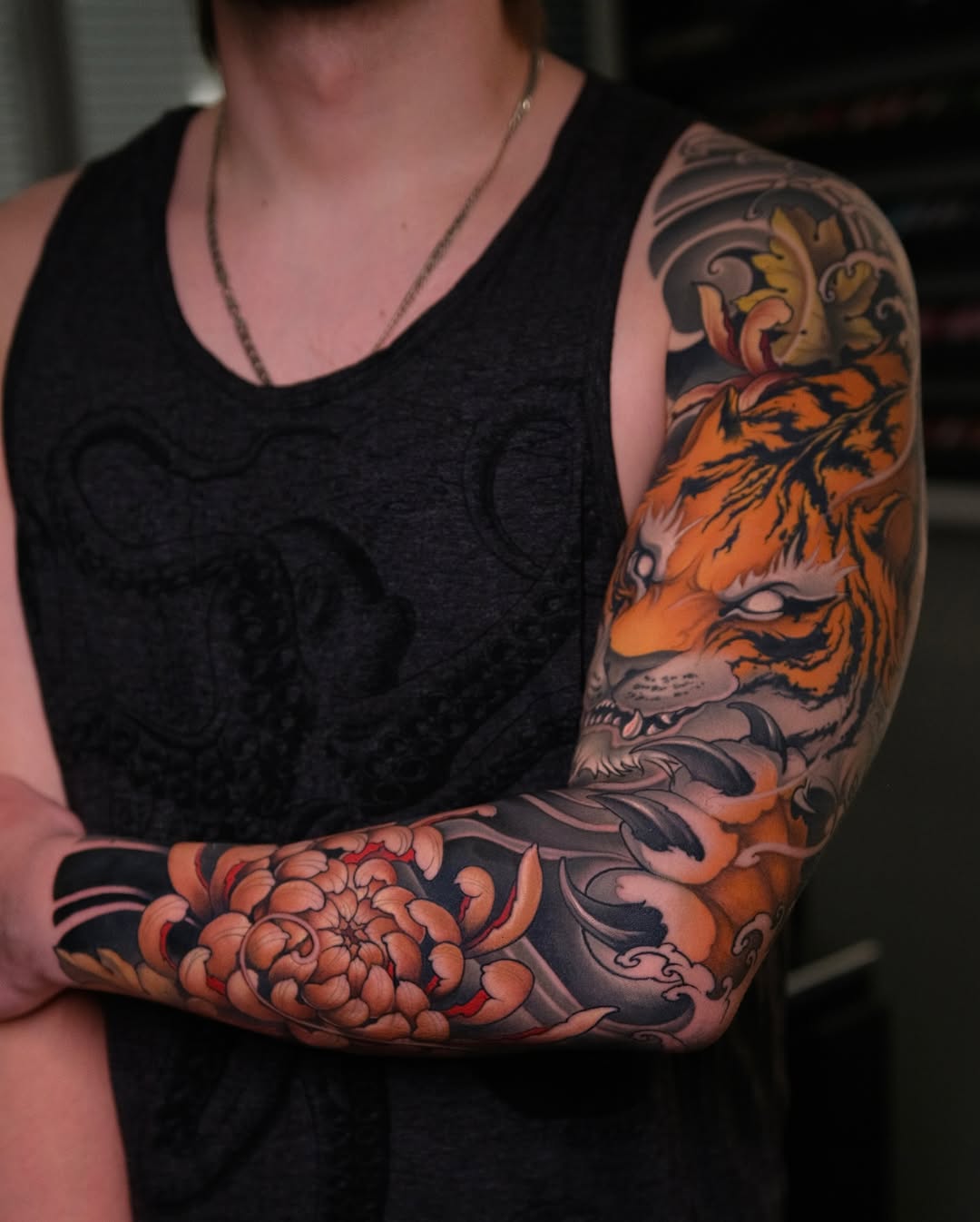 Full sleeve arm tattoo featuring an orange tiger head, red peony flower, and ornamental scrollwork in orange, black, and gray on pale skin.