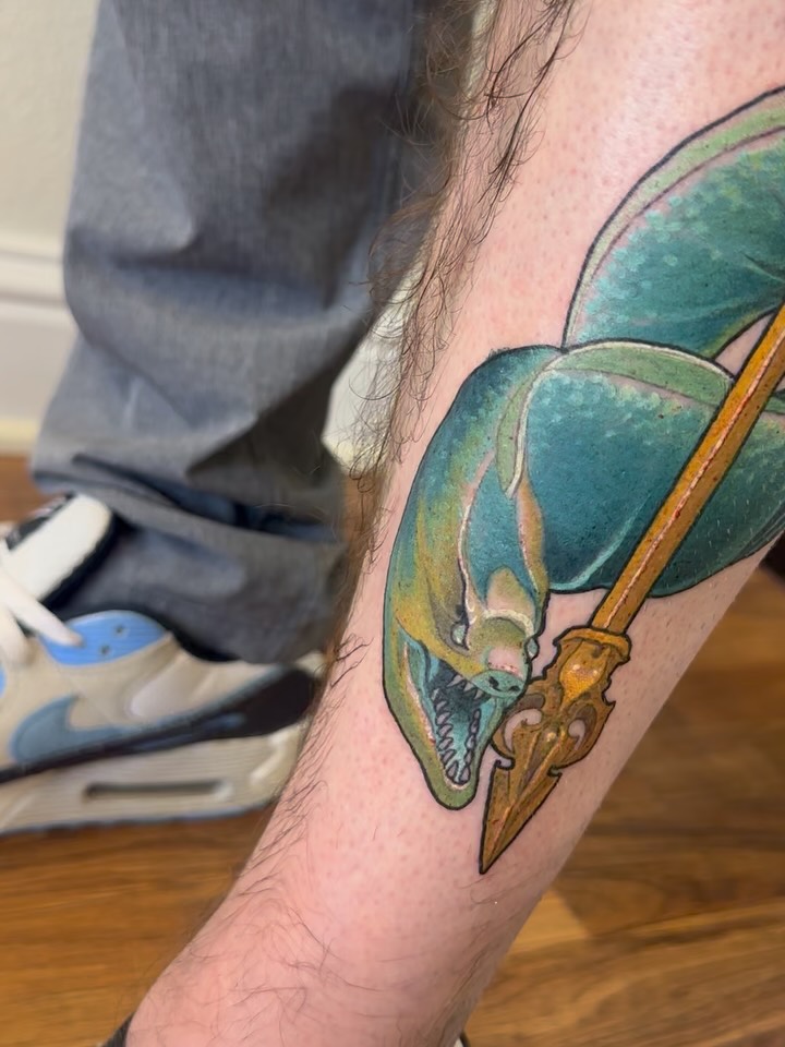 Colorful chameleon tattoo on the calf featuring green and teal hues with a brown branch, detailed eye and teeth visible.