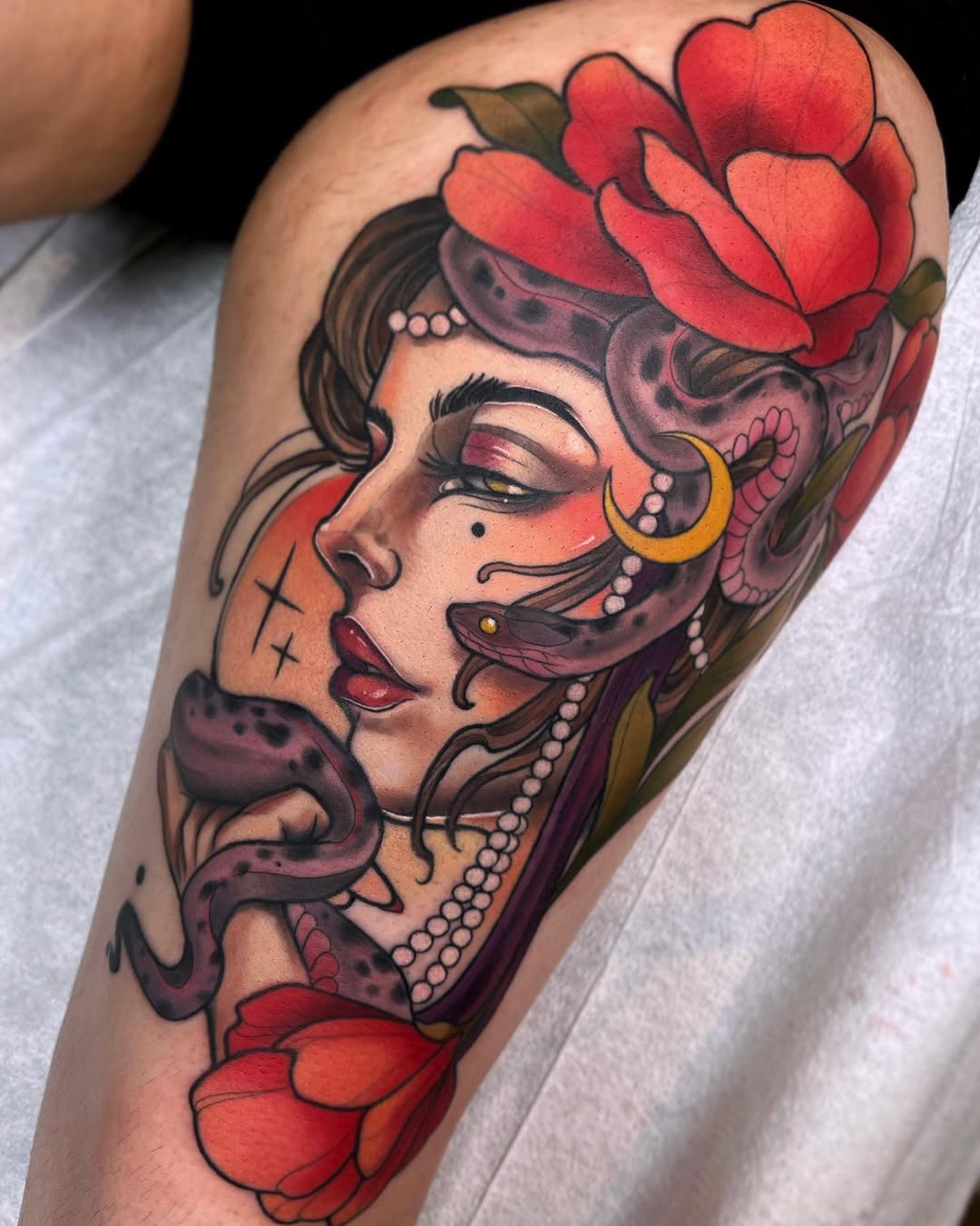 Colorful portrait tattoo on a calf featuring a woman's face with closed eyes, red flowers, gold crescent earrings, pearl necklace, and decorative facial markings.