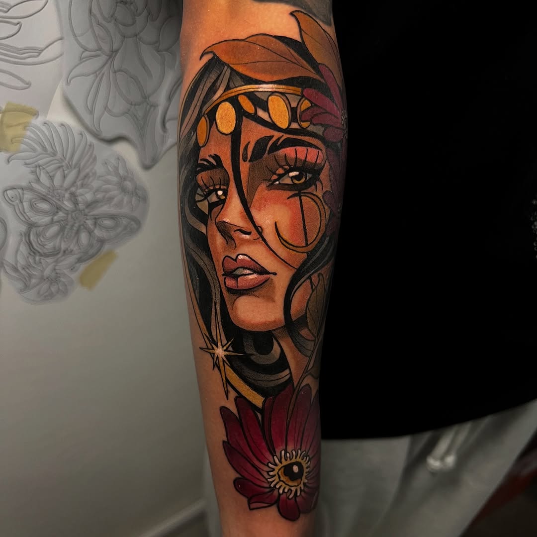Colorful arm tattoo featuring a woman's face with orange and gold tones, floral elements, and decorative details in warm reds and yellows.