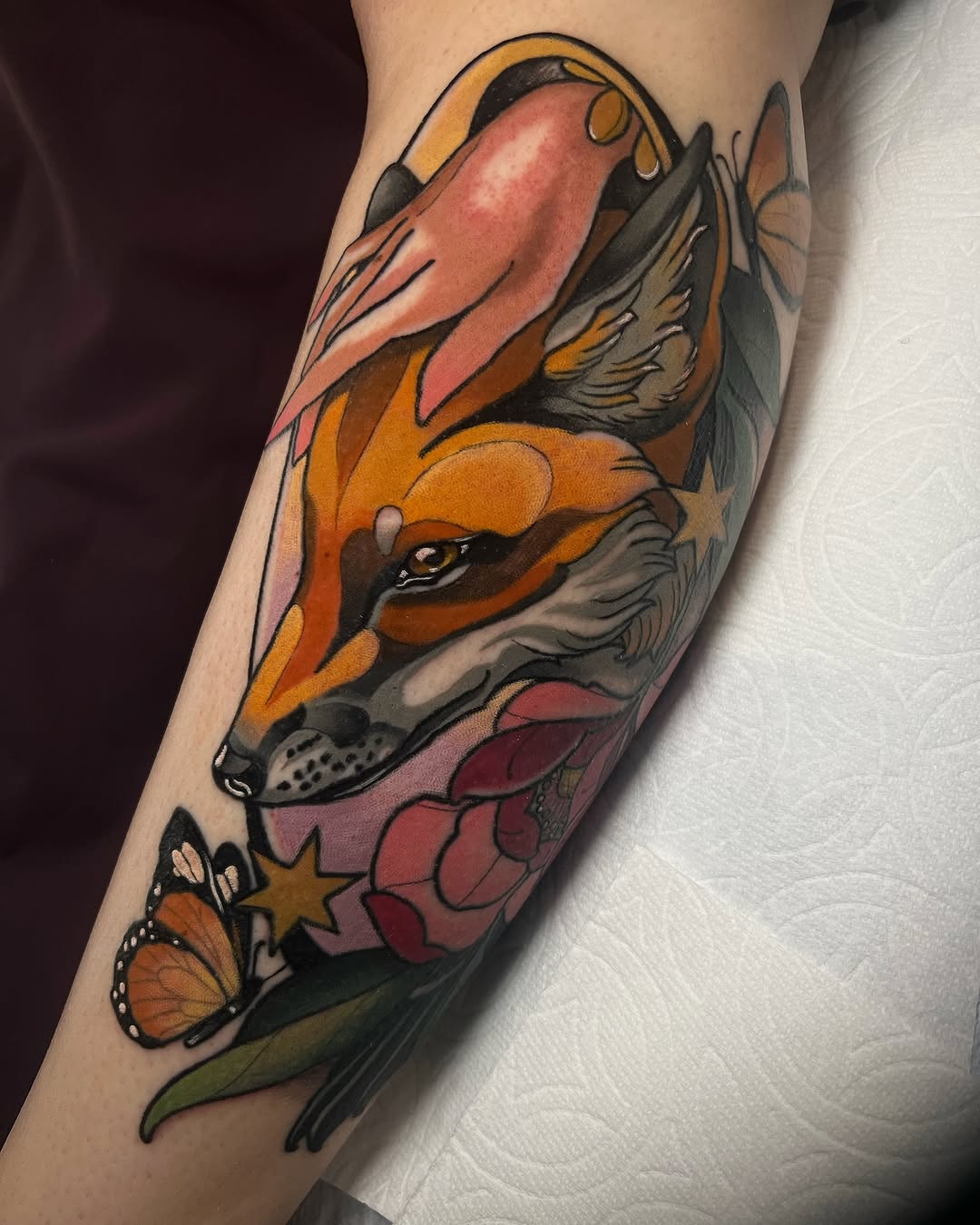 Colorful fox head tattoo on forearm featuring orange, gold, and burgundy tones with floral and butterfly elements below.