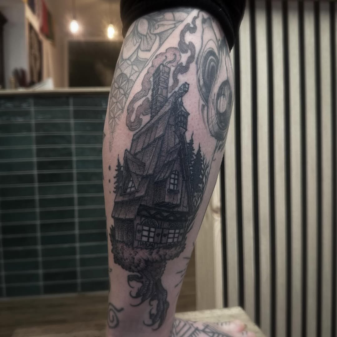 Haunted house tattoo on calf with twisted trees, ornate decorative elements, and celestial motifs in black ink.