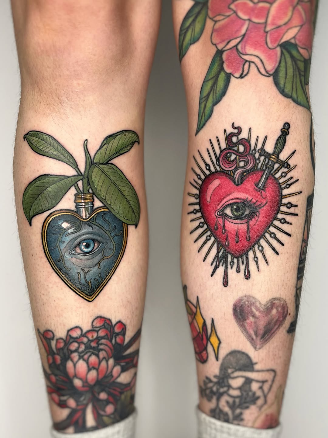 Two legs displaying matching heart-shaped designs with eyes and ornamental details, surrounded by floral elements in red, blue, green, and black ink.