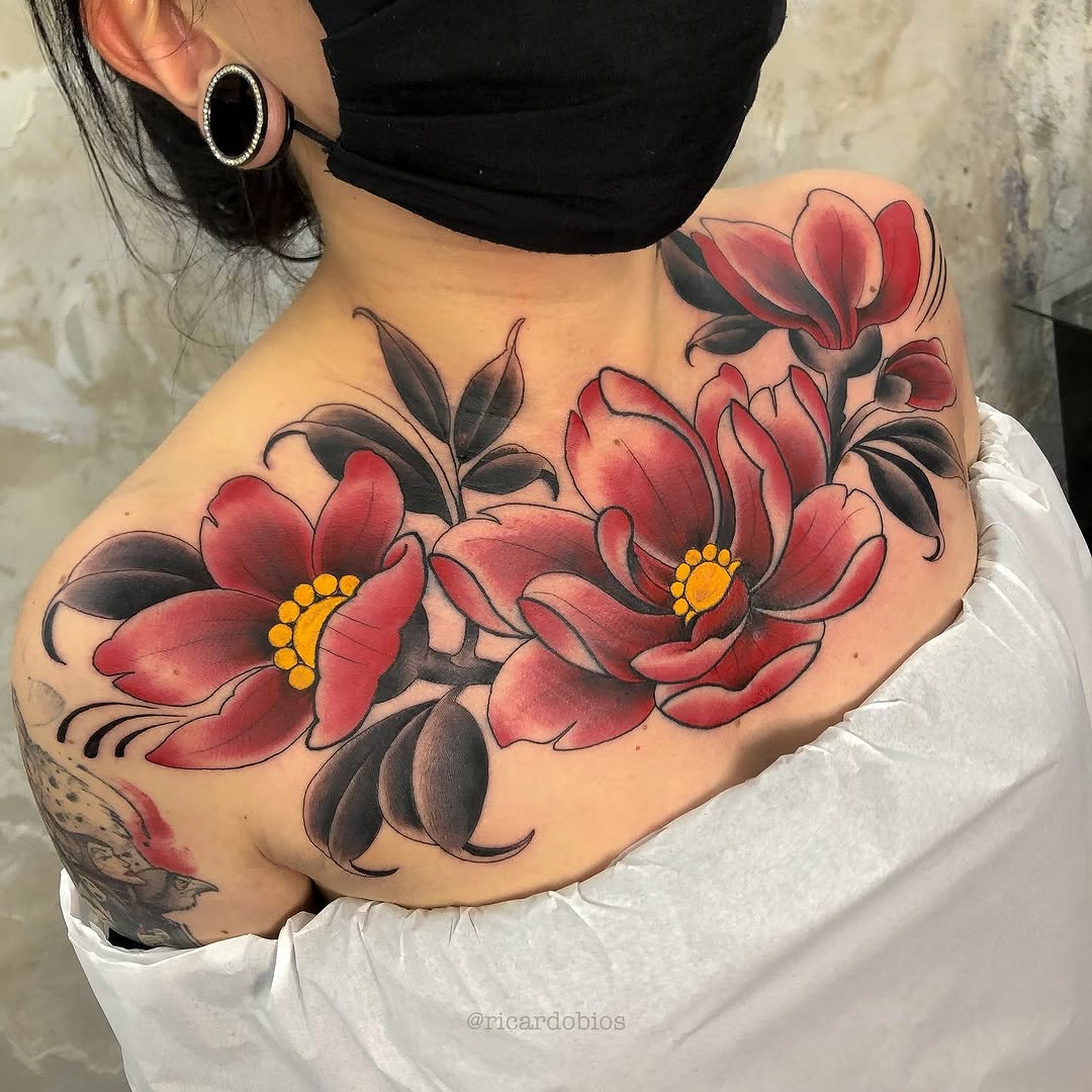 Red and pink flowers with dark green leaves and yellow centers tattooed on a person's shoulder and upper arm.