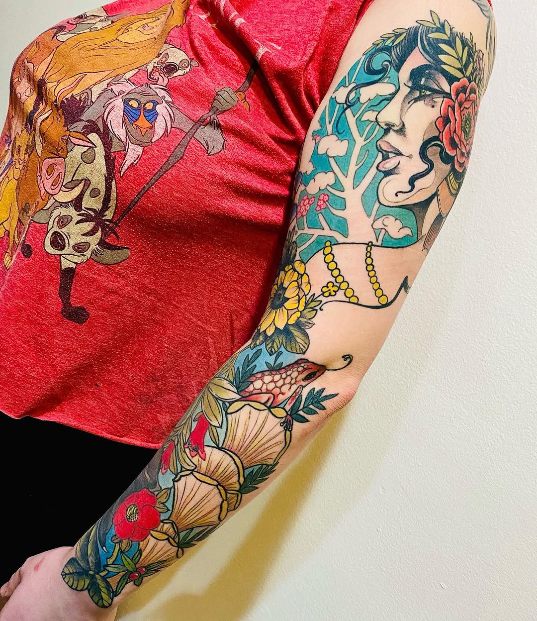 Full-sleeve arm tattoo featuring a stylized female face with floral elements, botanical designs, and decorative beads in vibrant colors including teal, coral, yellow, and red.