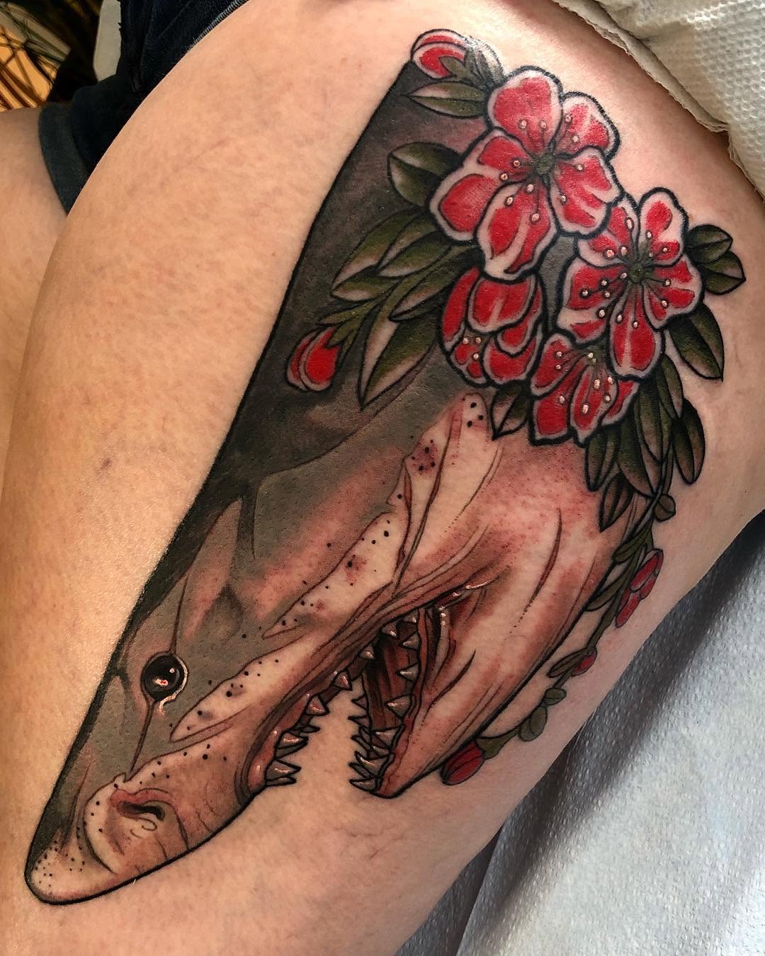 Shark head with open mouth holding red flowers and green leaves on upper arm, featuring red, green, black, and flesh tones.