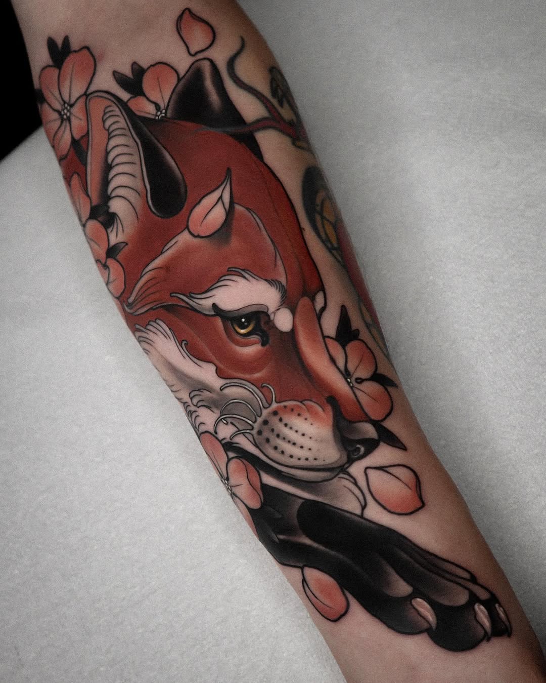 Red fox head with white facial markings surrounded by pink and black flowers on a forearm, with detailed shading and linework.