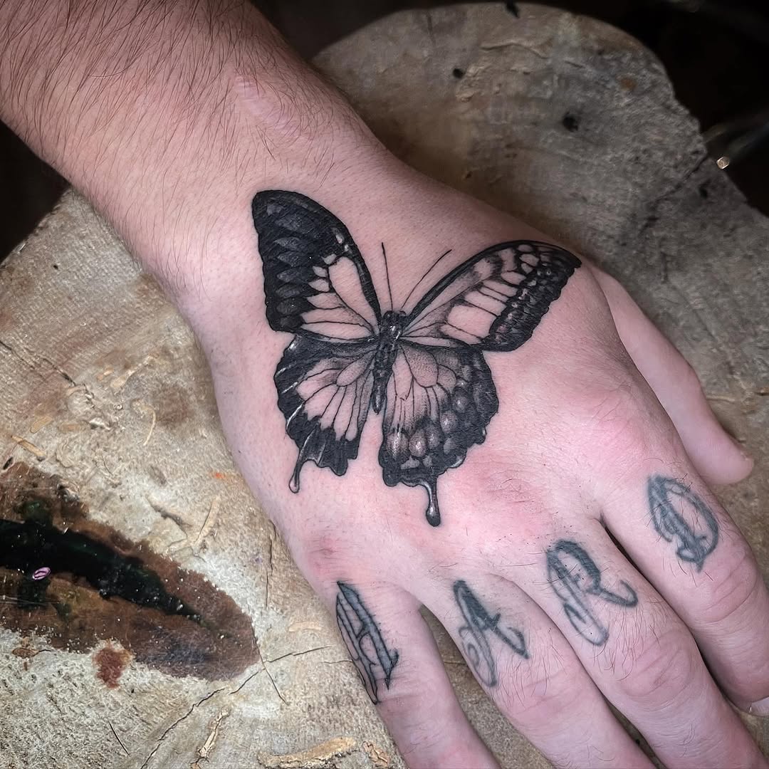 Black butterfly tattoo on the back of a hand with smaller linear designs on the fingers.