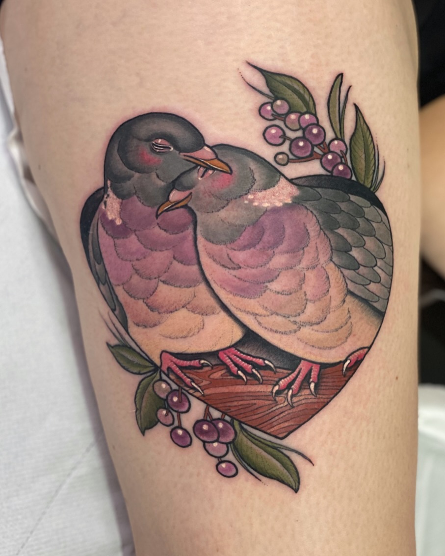 Two birds with pink and gray plumage perched on a brown branch surrounded by purple berries and green leaves, tattooed on the upper leg.