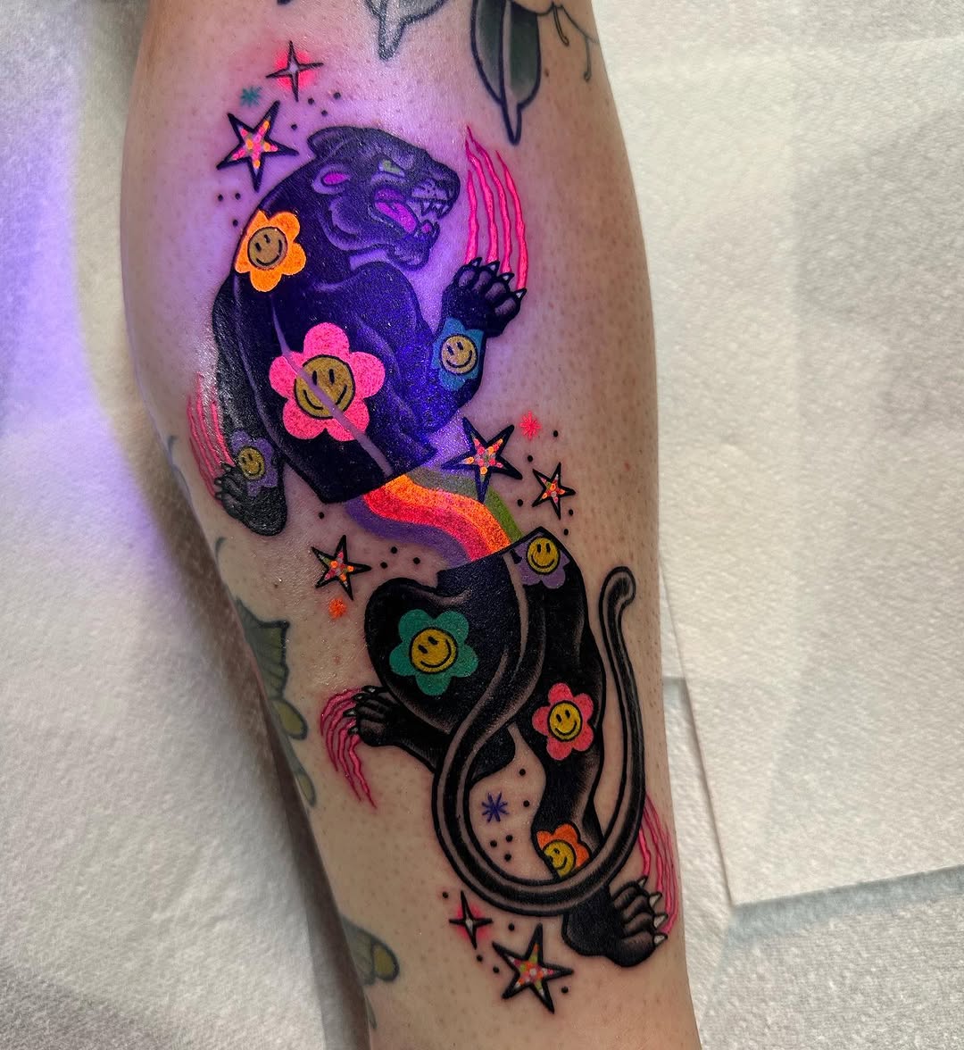 Two black panthers adorned with colorful smiley-face flowers and stars in neon pink, orange, and purple on the calf.