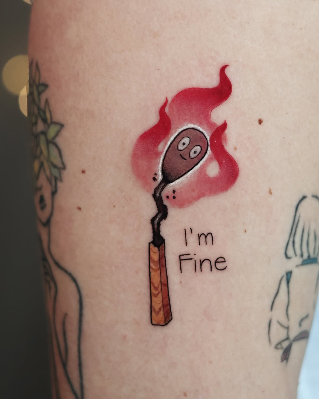 Tattoo on light skin featuring a smiling match stick character with a red flame head and text reading "I'm Fine" below.
