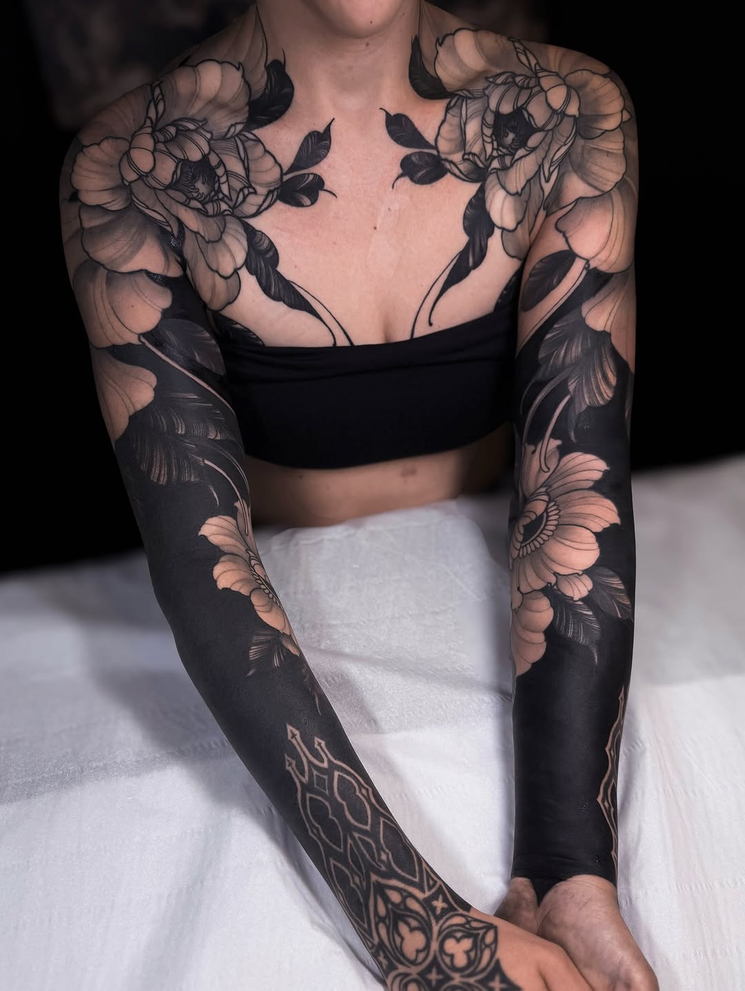 Full arm sleeve tattoos featuring peony flowers on shoulders and forearms with geometric patterns on wrists, rendered in black and tan ink.