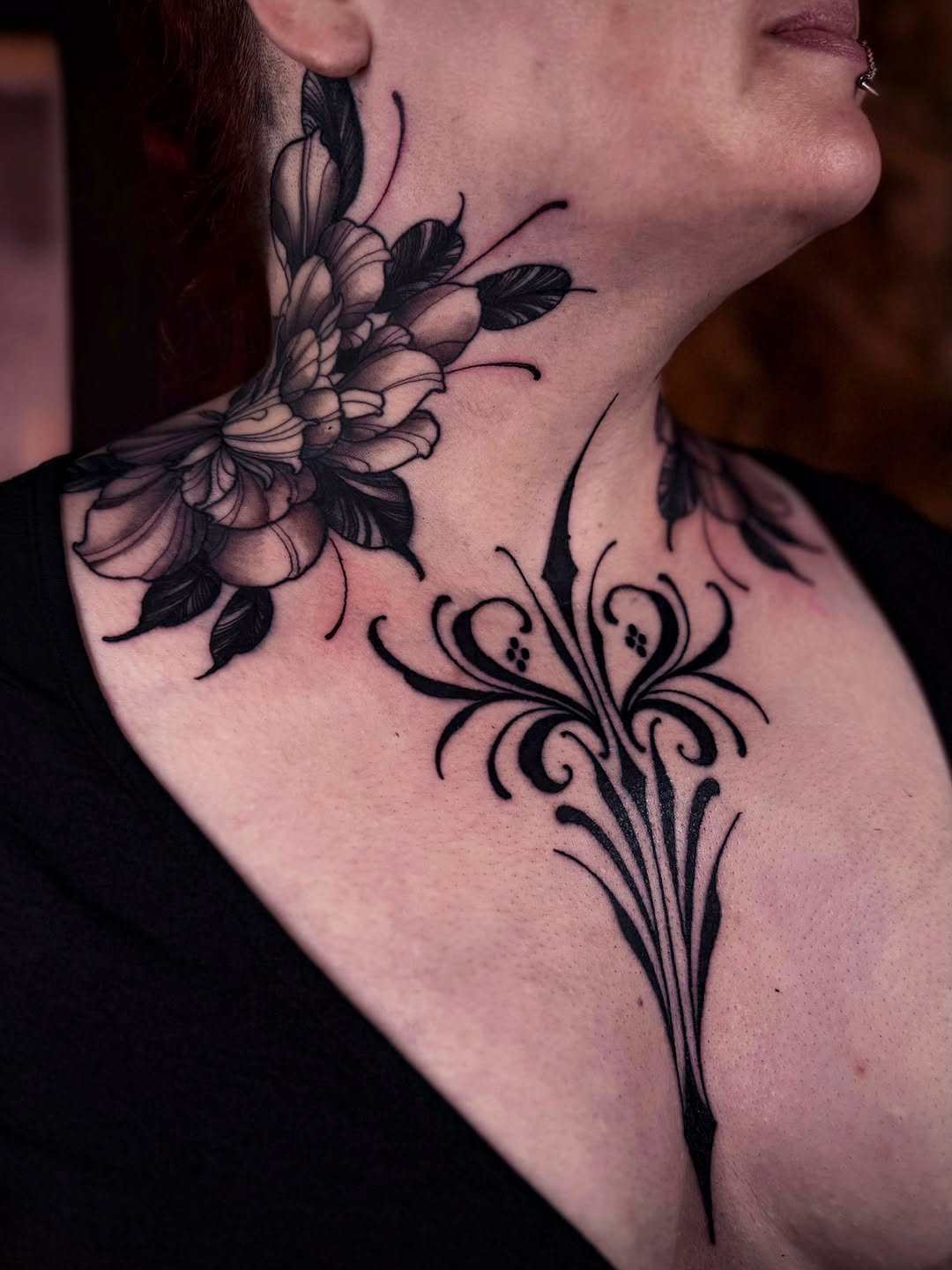 Detailed black floral tattoo on neck and upper chest featuring layered flowers with leaves and ornamental scrollwork designs.