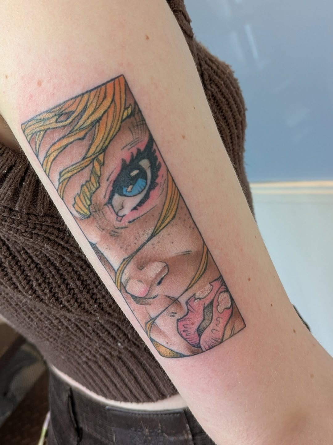 Colorful portrait tattoo on upper arm featuring a face with blonde hair and blue eyes, with pink and gold tones throughout the design.