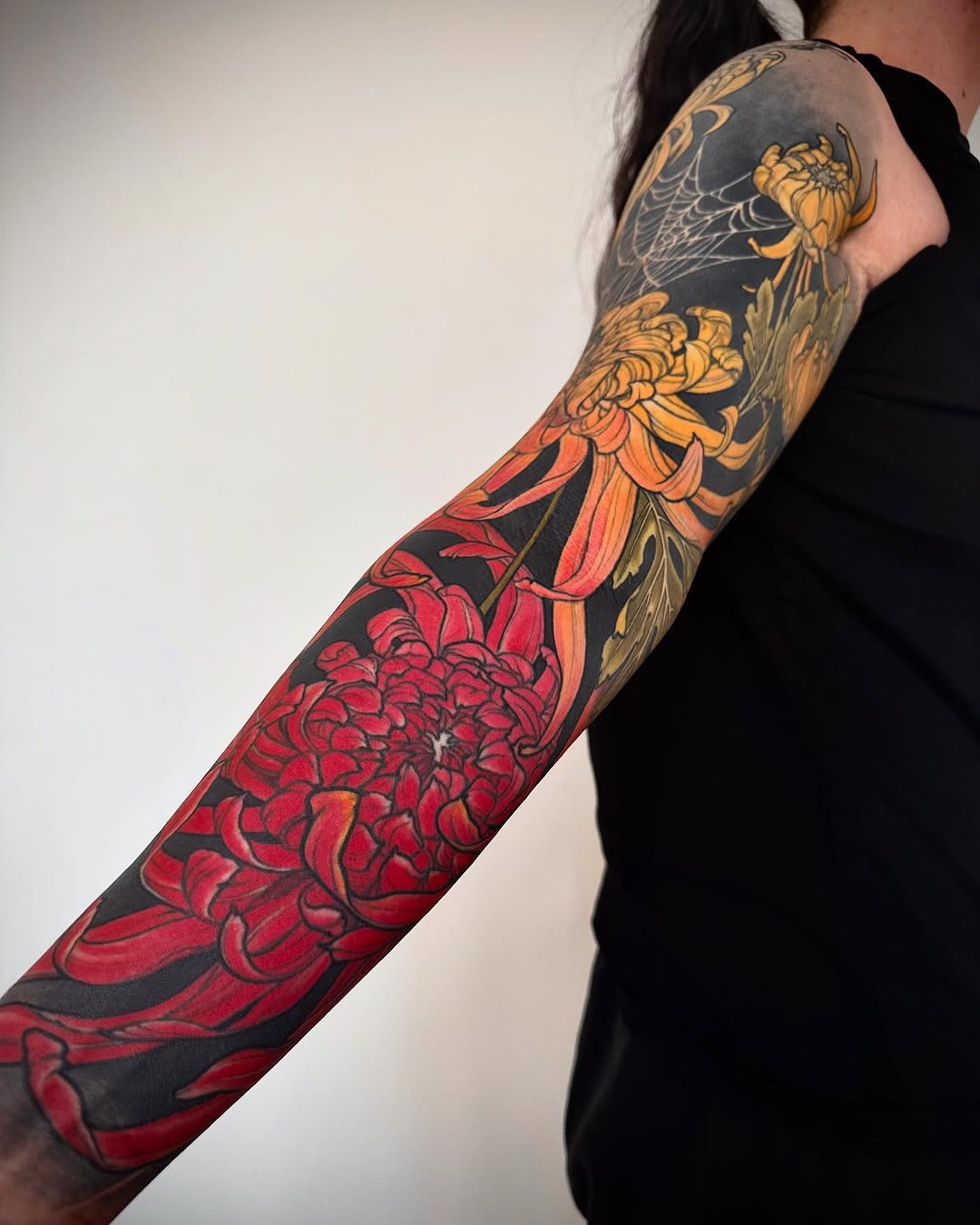 Full-length arm sleeve featuring chrysanthemum flowers in red, orange, and yellow with spider web details on the shoulder, dark background.