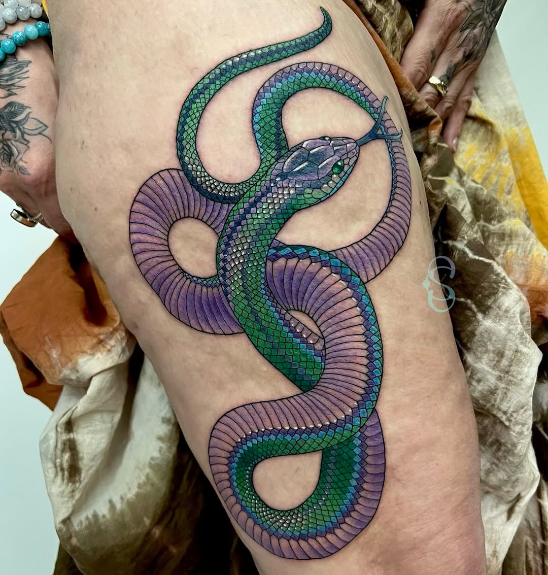 Colorful serpent tattoo on thigh featuring intertwined snakes with green scales and purple fins in shades of blue, green, and purple.