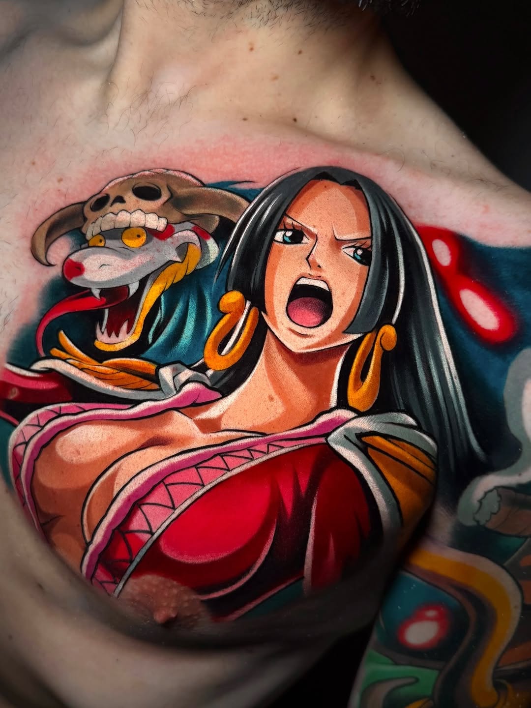 A colorful chest tattoo featuring a woman with long black hair and gold hoop earrings alongside a skeletal serpent creature in shades of orange, red, and teal.