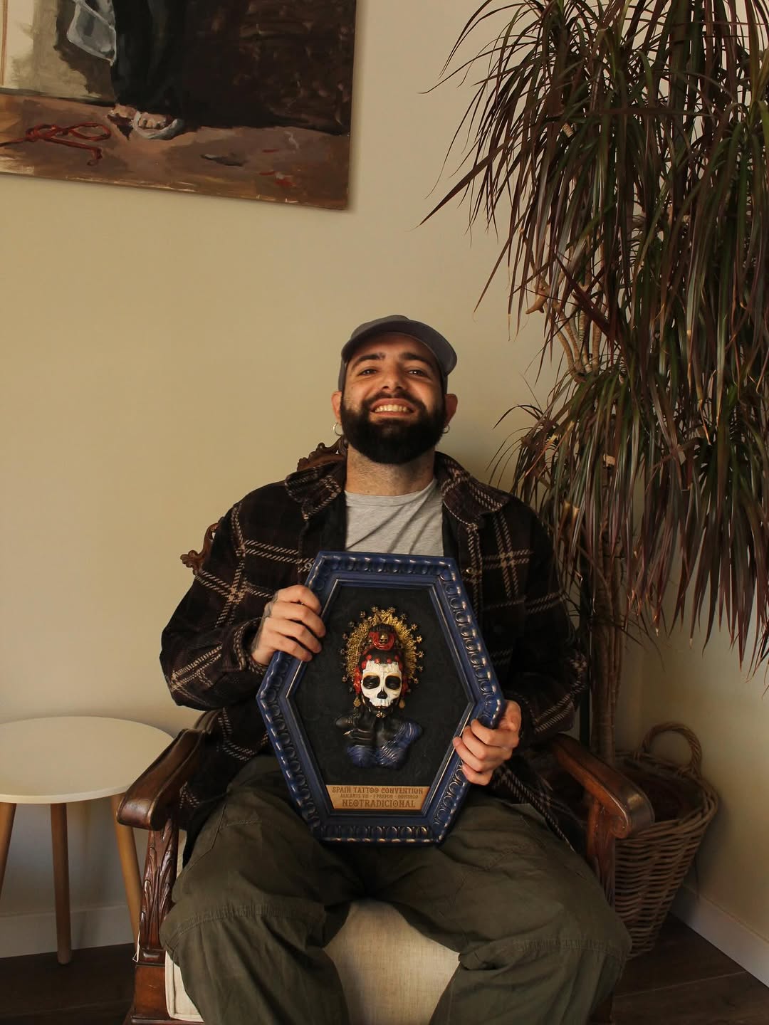 Man holding a coffin-shaped framed artwork displaying a skull with a red crown and ornate gold halo against a dark background.