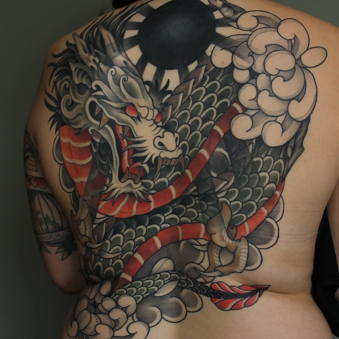 Large dragon tattoo covering the upper back with cream, black, red, and grey coloring, featuring ornate scales, flowing clouds, and detailed facial features.