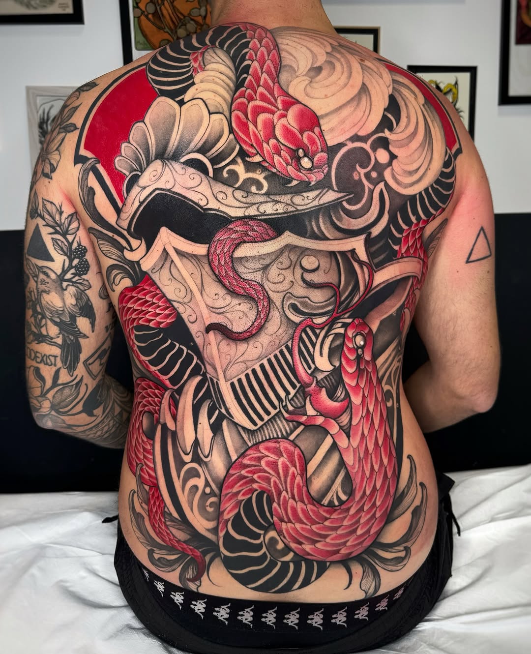 Back tattoo featuring a skull with ornate decorative flourishes, red flowers, and black striping across the chest and torso.