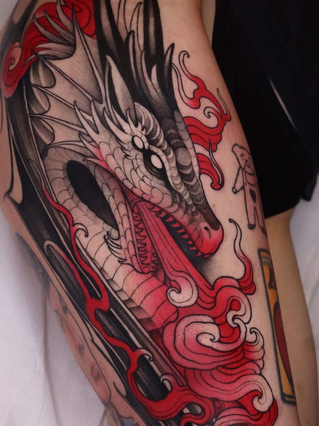 Dragon head tattoo on the leg featuring gray scales, red ornamental flames, and black line work with detailed shading and decorative scrollwork elements.