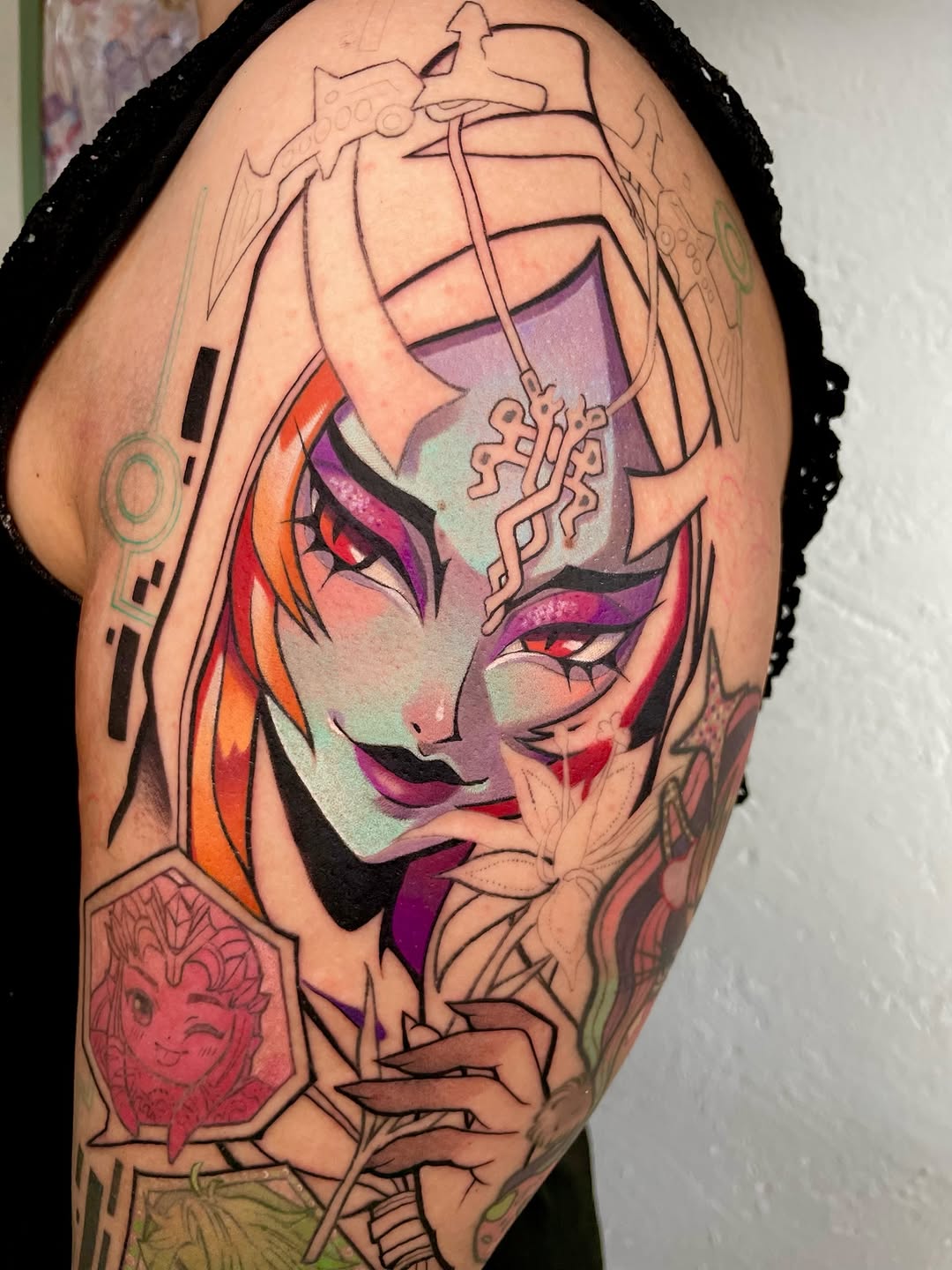 Colorful portrait tattoo on upper arm featuring a face with purple and orange sections, geometric patterns, and decorative elements in red, pink, and green.