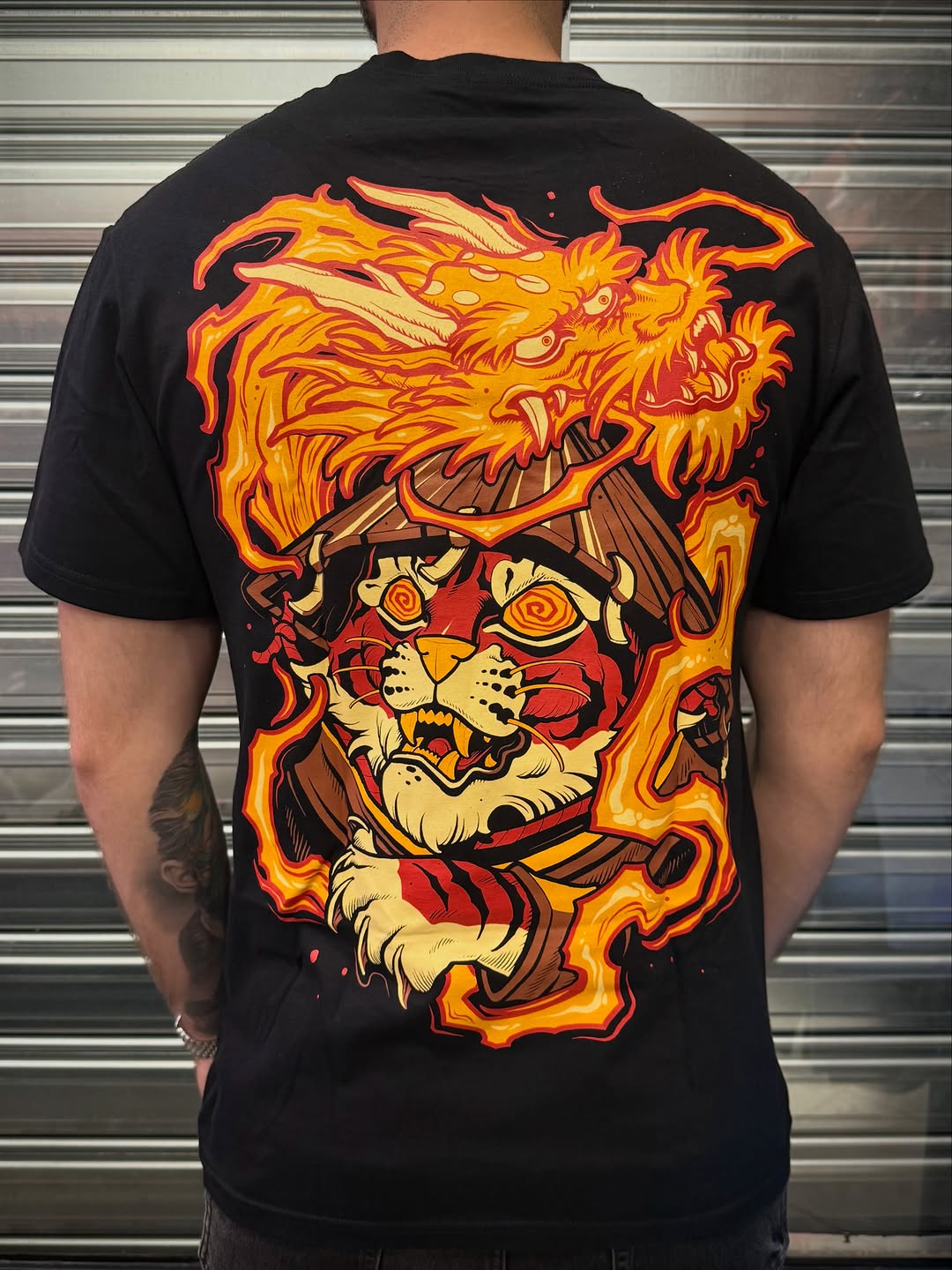 Back tattoo featuring a fierce tiger head with flames surrounding it in orange, yellow, and red tones on black fabric.