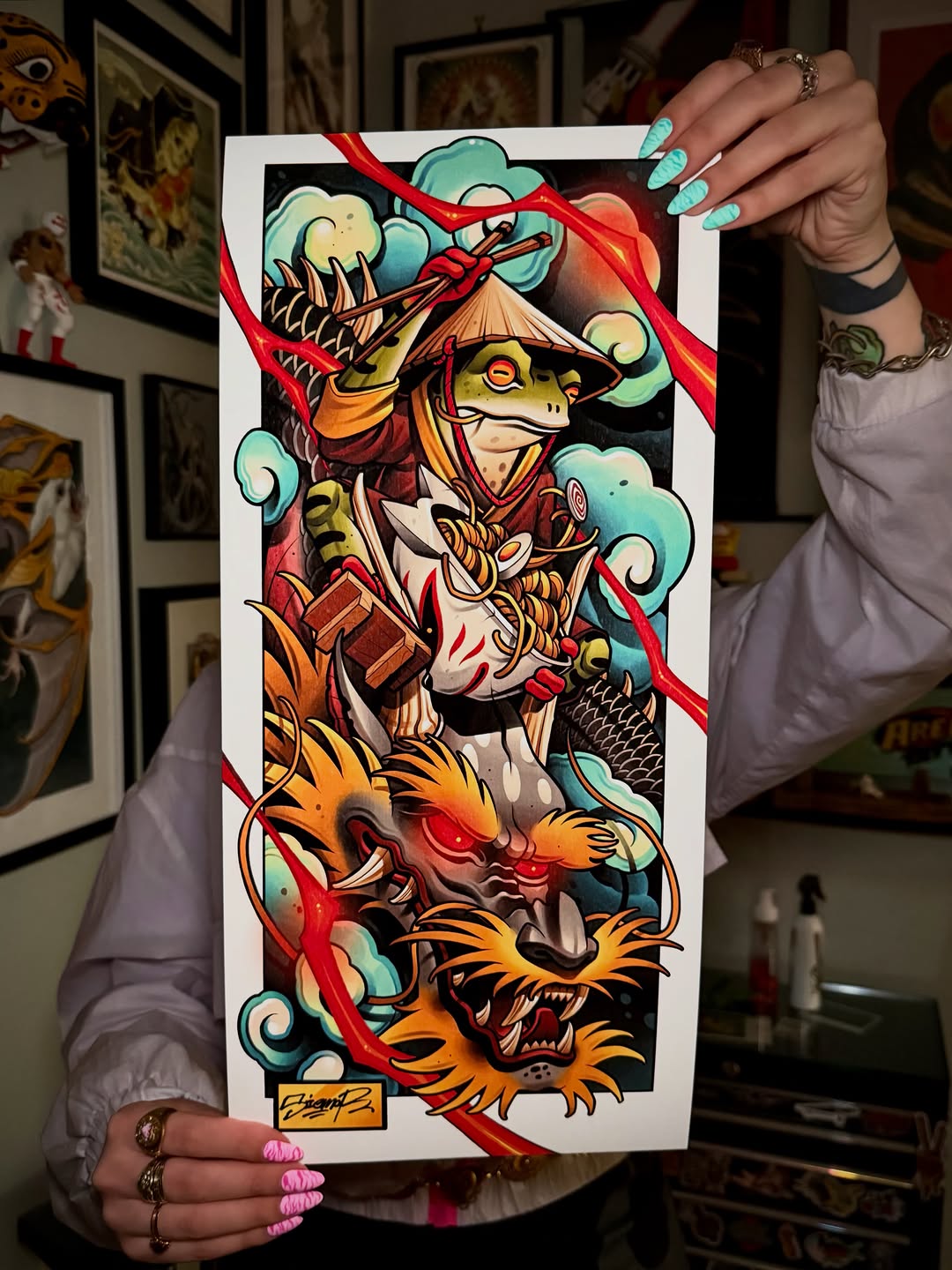 Colorful tattoo design featuring a frog warrior in red robes with dragons and clouds, displayed on white paper with red ribbon.