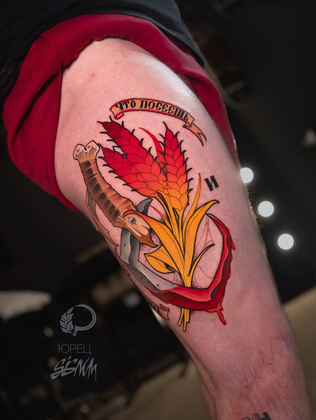 Colorful arm tattoo featuring a goat holding a red flower with yellow center and spiky red petals, with Cyrillic text on a banner above.