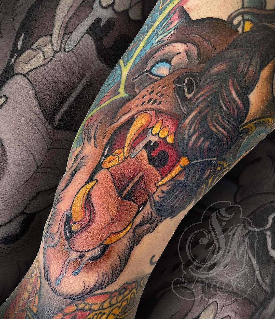 Colorful lion head tattoo on forearm featuring brown fur, blue eyes, red and yellow mouth details, and decorative gold accents.