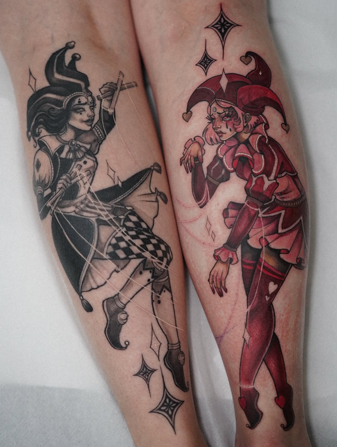 Two leg tattoos featuring ornate female figures in contrasting black and red color schemes, adorned with decorative stars and geometric elements.