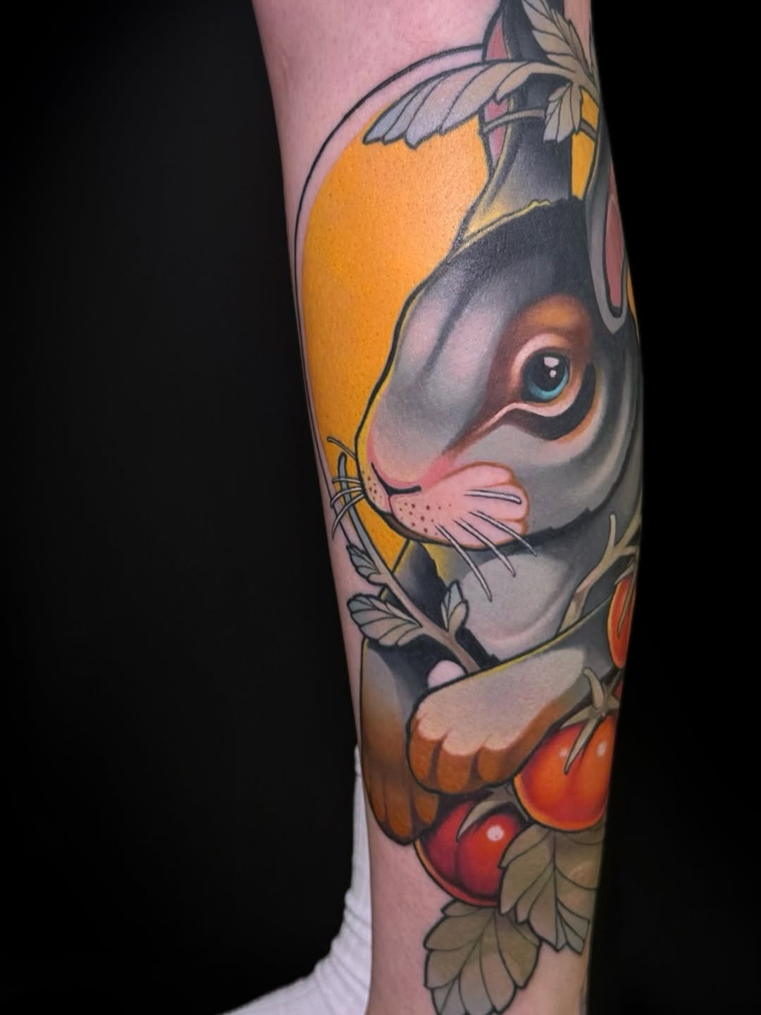 Colorful rabbit tattoo on forearm featuring gray and orange tones with red flowers and green leaves, displaying detailed facial features and whiskers.
