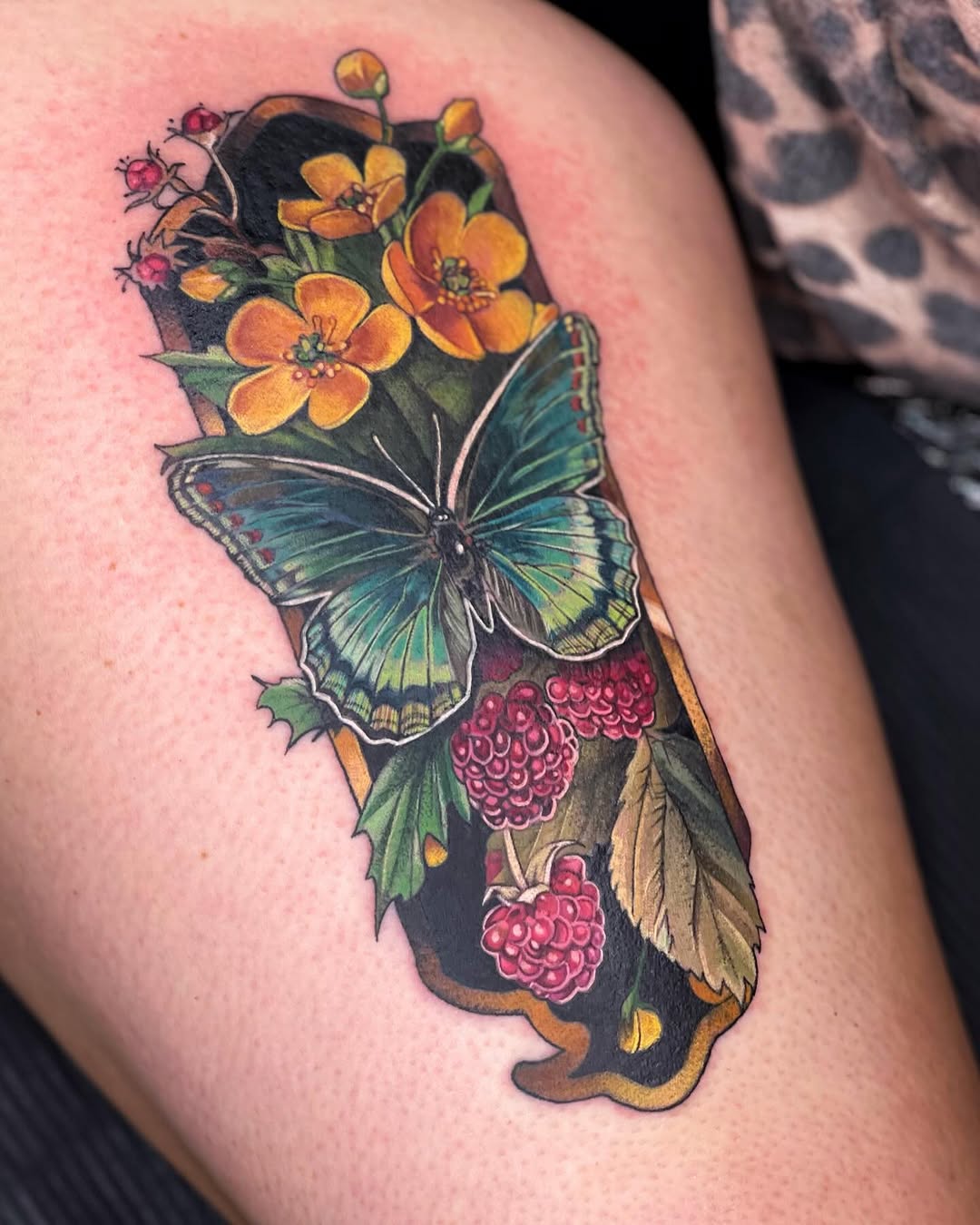 California state map filled with orange flowers, red raspberries, green butterfly, and dark background, tattooed on upper arm.