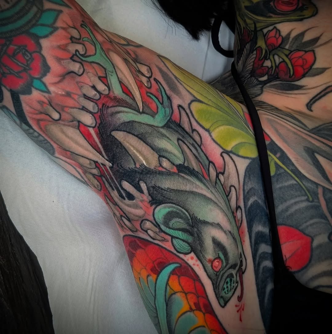 Colorful deer head tattoo on upper arm with red roses, green vines, yellow accents, and ornamental details in red, green, yellow, and black ink.