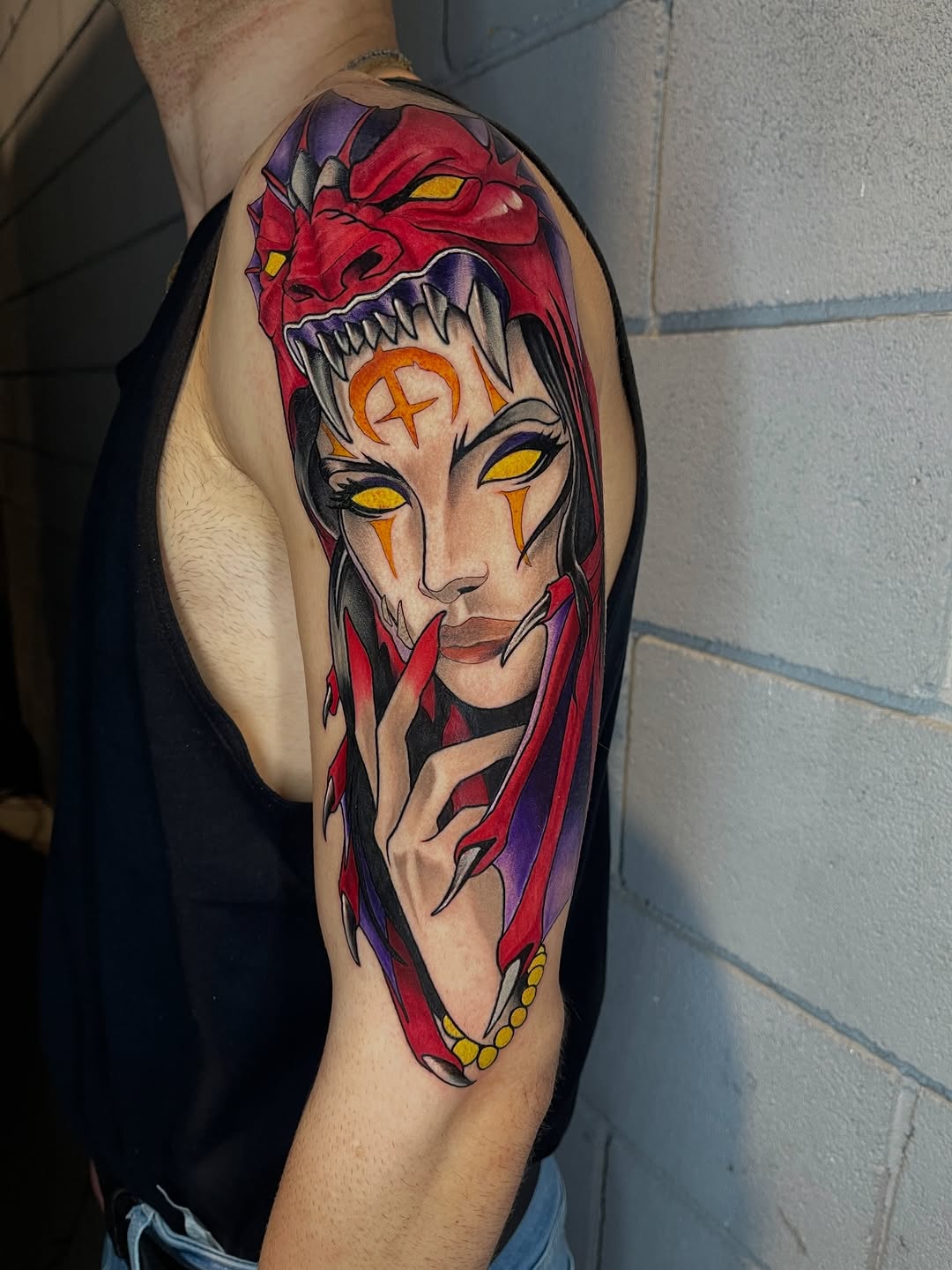Colorful arm tattoo featuring a split-faced demonic figure with yellow eyes, red skin, sharp teeth, and flowing hair in red and purple tones.