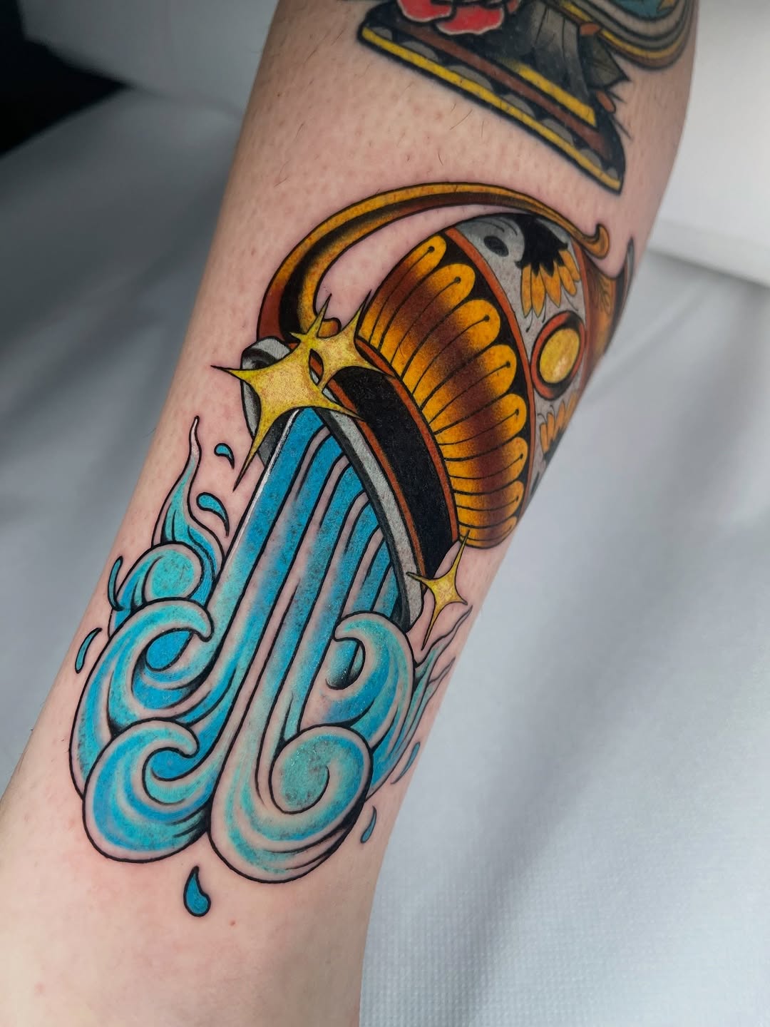 Colorful tattoo on forearm featuring a butterfly with yellow and orange wings above ornate turquoise water swirls and a small teardrop detail.