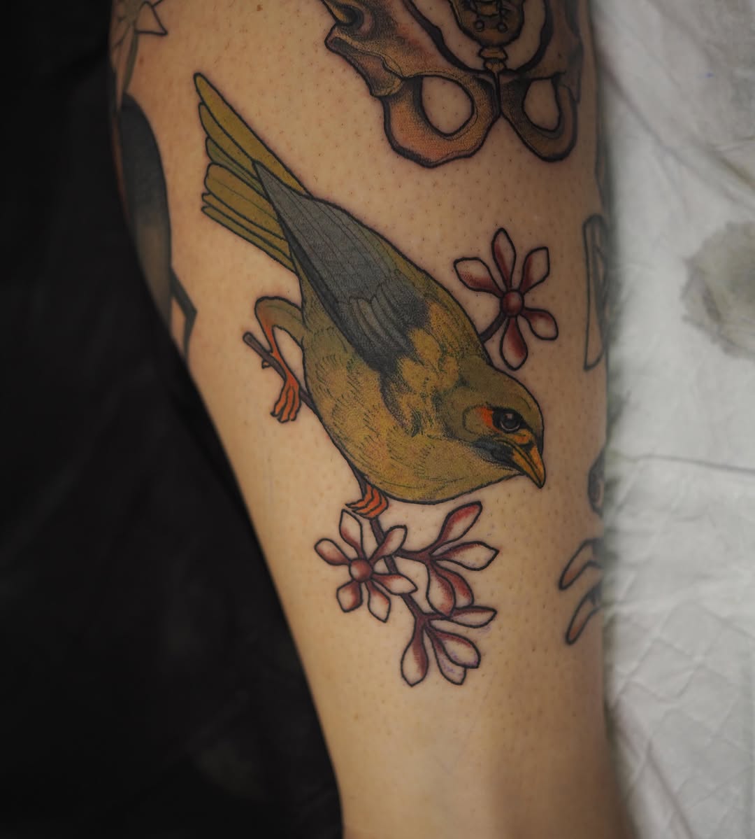 Colored bird tattoo with golden-brown plumage and dark wings positioned on upper arm, surrounded by pink and red flowers.