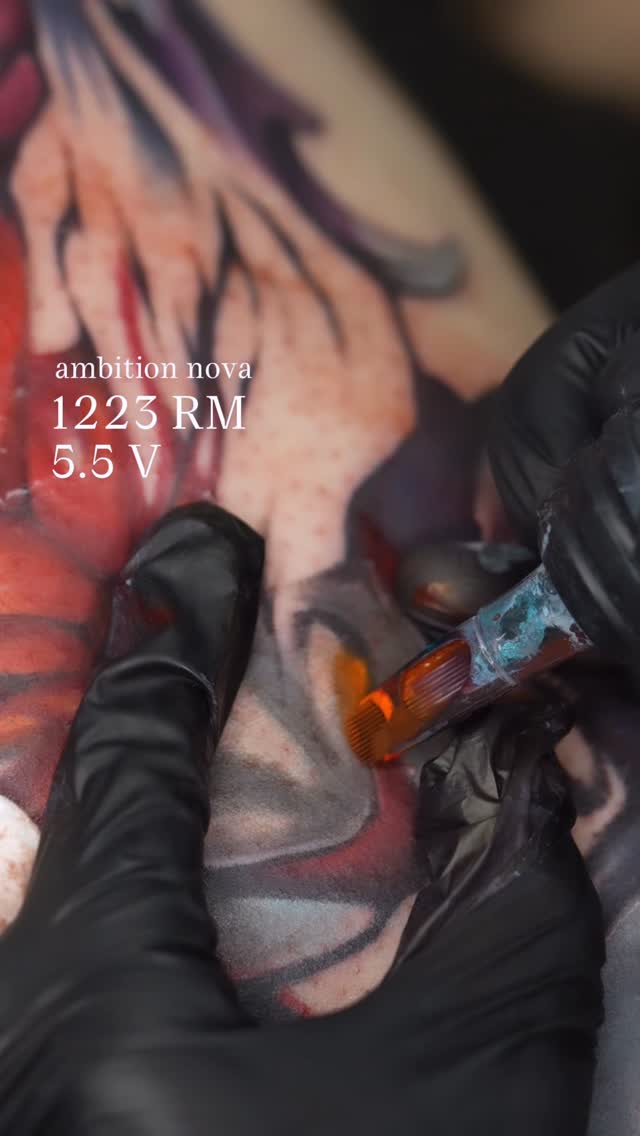 Tattoo artist applying red and purple colored ink to a client's hand using an Ambition Nova machine at 1225 RM and 5.5V settings.