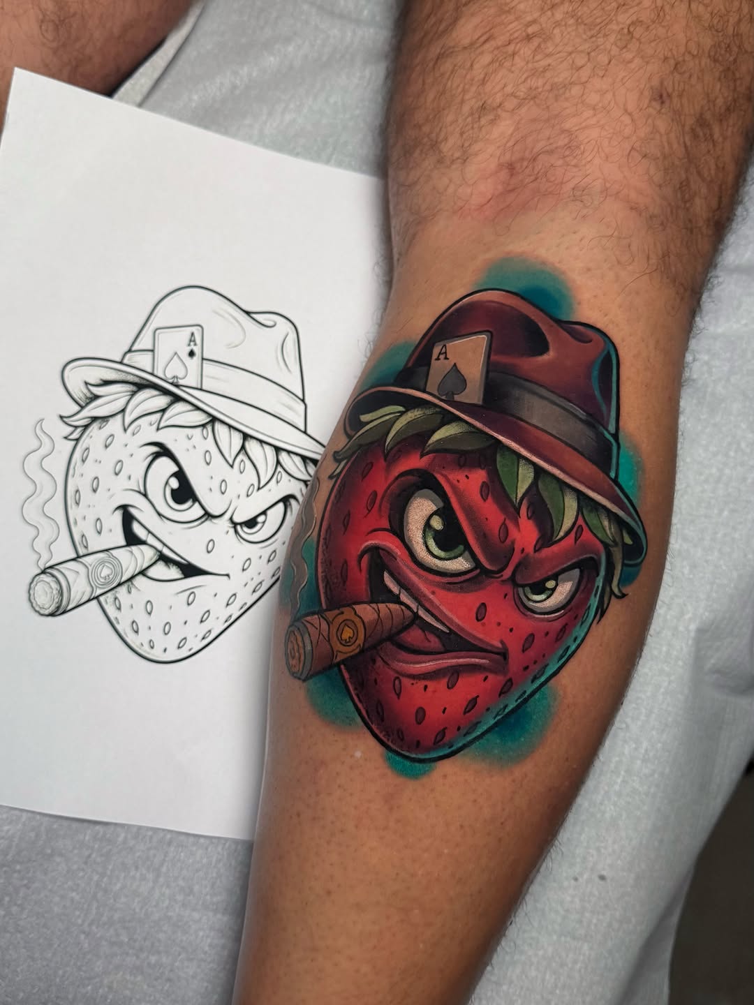 Strawberry character with playing card hat and cigar on forearm, colored in red with teal and burgundy shading, displayed next to black-and-white sketch.