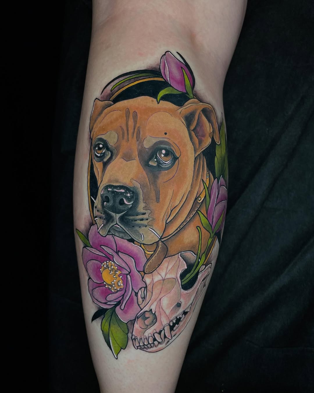 Brown dog's head portrait with pink flowers and a skull integrated below, tattooed on a calf with orange, purple, green, and black colors.