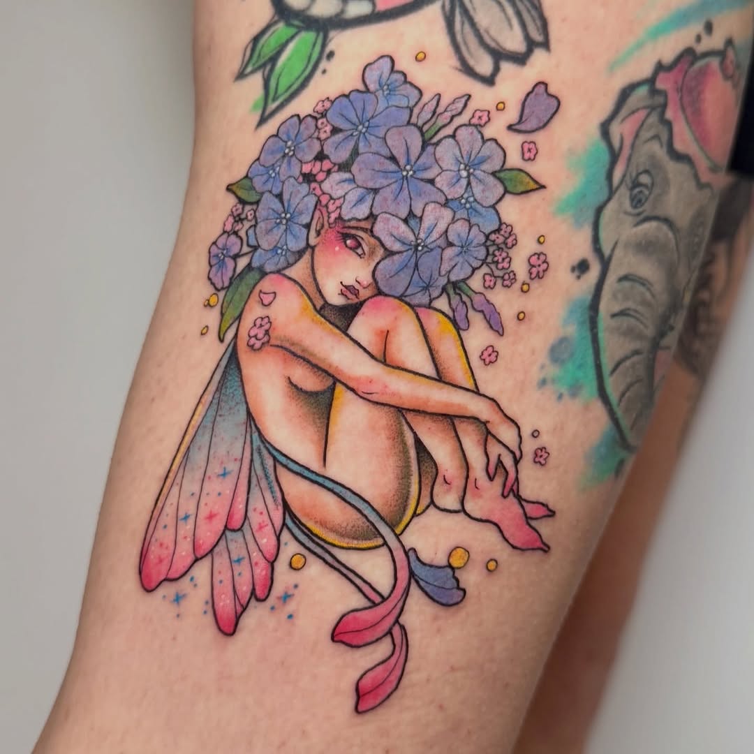 Fairy figure with purple flower hair and pink wings on upper arm, featuring blue, yellow, and pink colored ink details.