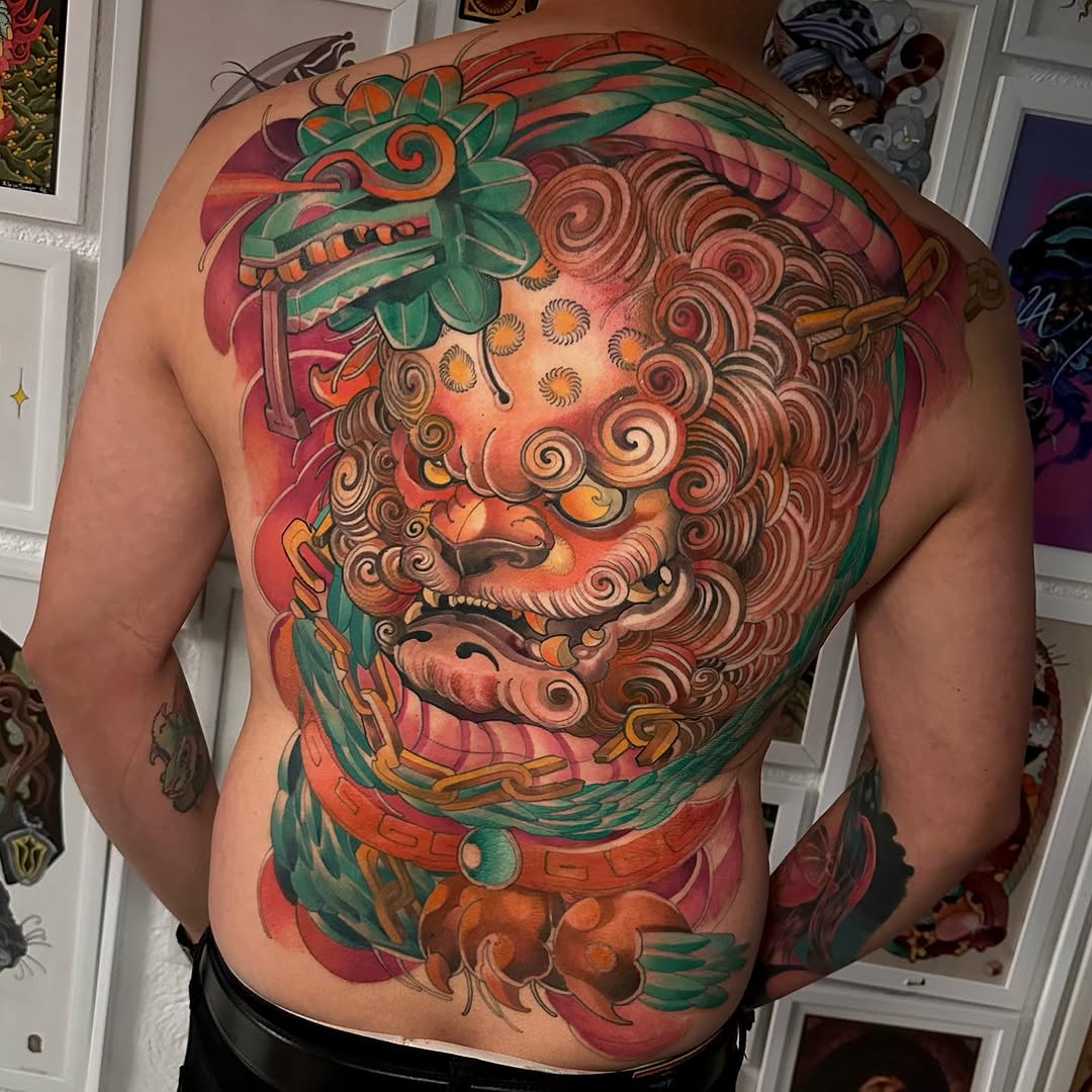 Large colorful back tattoo featuring a bearded face with ornate spiral hair, green foliage, and red background elements on a shirtless male torso.