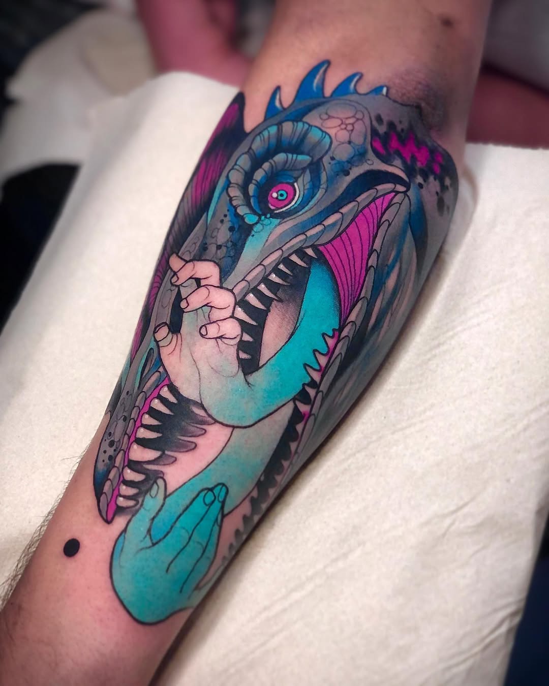 Colorful bird tattoo on forearm featuring cyan, magenta, and pink hues with detailed feathers, open beak, and prominent eye.
