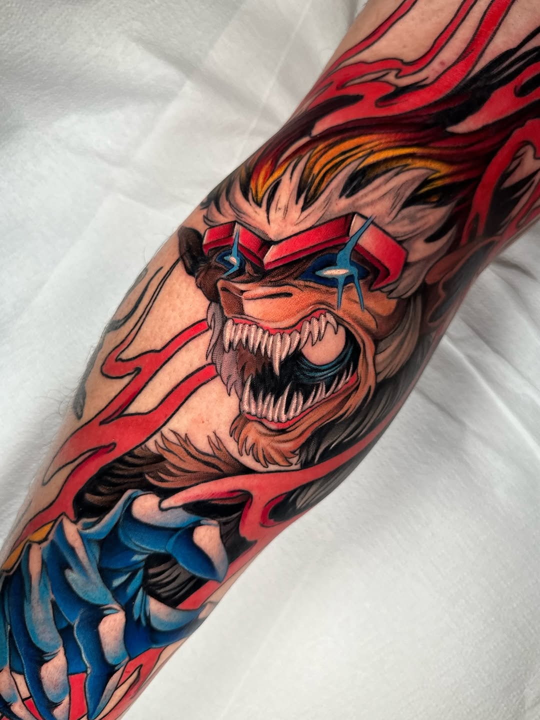 Colorful tattoo on an arm featuring a fierce bearded character with red hair, blue eyes, red headband, and blue clothing surrounded by red flames.